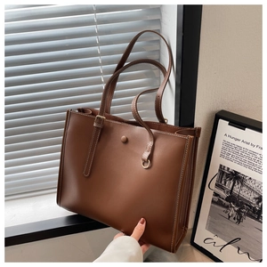 Detail of dark brown leather tote bag with white contrast stitching and adjustable strap