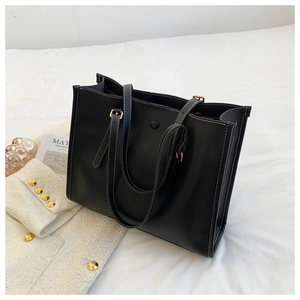 Detail of black leather tote bag featuring contrast white stitching and handle detail