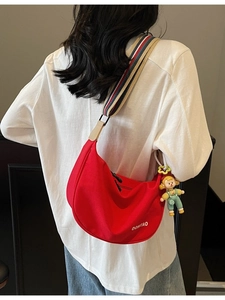 Red half-moon canvas crossbody bag with wide striped strap and cartoon pendant