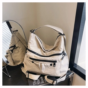 Detail of off-white nylon tote bag showing multiple black zippers and wrinkled texture