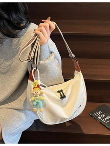 White canvas half-moon dumpling crossbody bag with a colorful wide strap and cartoon charm
