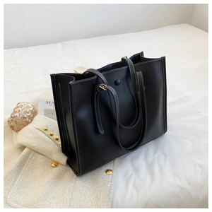 Detail of black leather tote bag with white contrast stitching and gold buckle