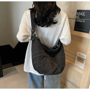 Detail of dark denim crossbody bag featuring contrast stitching and front patch pockets
