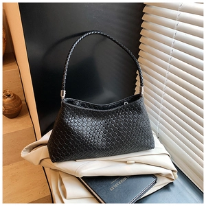 Détail du sac à bandoulière en cuir tressé noir sur un fond de blazer élégant et chic