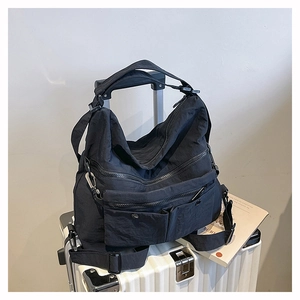 Detail of black nylon multi-pocket tote bag placed on a white rolling suitcase in a travel scene