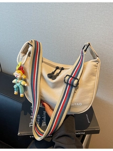 Beige dumpling crossbody bag with wide striped strap and cartoon charm on a book