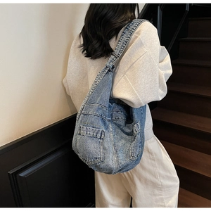Detailed view of washed blue denim crossbody bag featuring functional outer cargo pockets