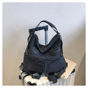 Detail of black nylon tote bag with multiple zipper pockets on a white suitcase