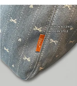 Detail of blue denim fabric with bow and heart prints featuring an orange woven label