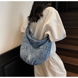 Macro view of large washed blue denim crossbody bag with practical dual front pockets