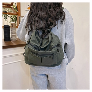 Detail of dark green nylon multi-pocket tote bag showing adjustable metal buckles and straps