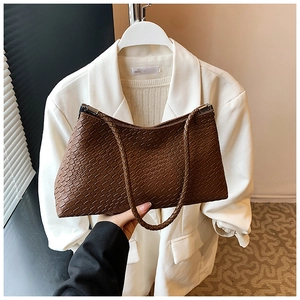 Détail d'un sac sous le bras marron tissé avec poignée tressée et garnitures métalliques