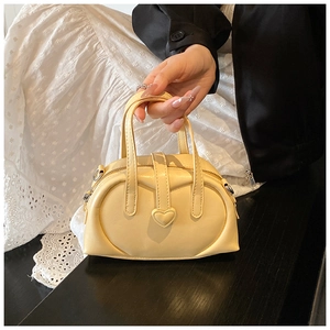 Detail of light yellow leather pillow bag with heart-shaped buckle and hand-held handle