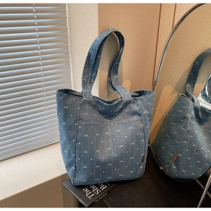 Macro detail of blue denim tote bag with white bow patterns and brown leather label