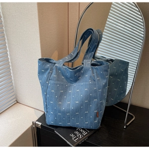 Detail view of denim tote bag featuring white heart and bow prints with a front pocket