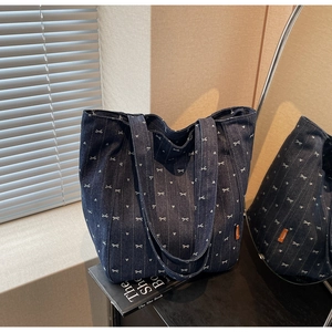 Detail of blue denim tote bag with white bow and heart prints in natural light setting