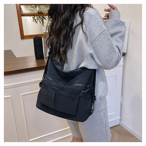 Close-up of a large black multi-pocket crossbody tote bag worn by a model in a cafe