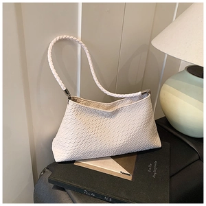 Gros plan sur la texture tressée d'un sac bandoulière blanc posé sur un livre noir