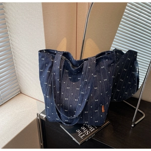 Detail of blue denim tote bag with white bow and heart embroidery on a black surface