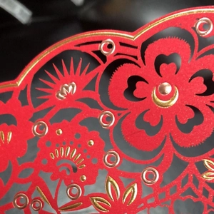 Intricate laser-cut red cardstock with gold foil floral patterns for wedding decor