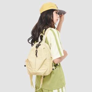 Détail d'un sac à dos en nylon crème avec fermeture éclair verticale et poches latérales