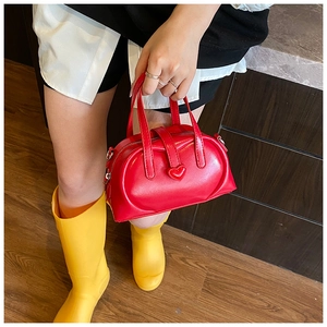 Detail of red leather pillow handbag featuring a 3D heart-shaped lock and dual zippers