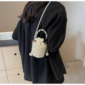Detail of woven faux pearl bucket bag with satin drawstring liner and long chain strap
