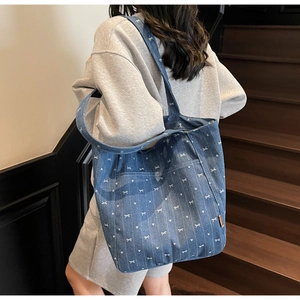 Detail of casual denim tote bag with white bow patterns worn by model on stairs
