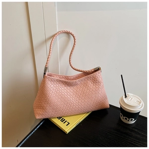 Détail d'un sac à bandoulière en cuir tressé rose posé sur des livres avec style