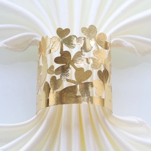Close-up of gold clover laser-cut napkin ring on a folded white fabric napkin