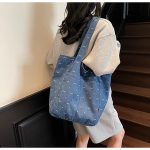 Blue denim tote bag with white bow and heart prints shown on a model in a modern interior