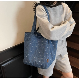 Close-up of denim tote bag featuring white bow heart print and side pocket detail