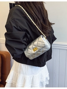 Sac bandoulière matelassé argenté avec chaîne dorée porté par un mannequin en extérieur