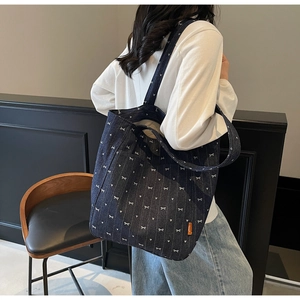 Close-up of denim tote bag with white bow and heart prints and orange woven label detail
