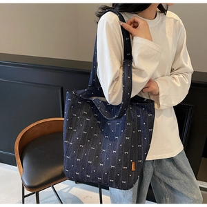Detail of blue denim tote bag featuring white bow patterns and orange woven side label