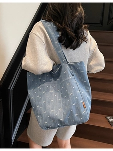 Blue denim tote bag with white bow pattern and side pocket on a model standing on wooden stairs