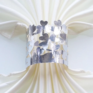 Macro shot of silver clover heart cutout napkin ring on white satin fabric texture