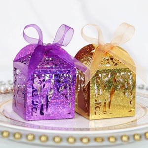 Detail of laser-cut wedding favor boxes with glitter finish and sheer ribbons on a porcelain plate