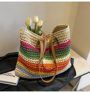 Close-up of rainbow woven straw tote bag with brown leather straps on wooden table