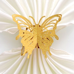 Golden laser-cut glitter butterfly napkin rings on white satin fabric for wedding decor