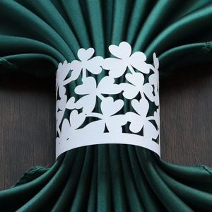 Detailed laser-cut white clover paper napkin ring on a dark green satin napkin