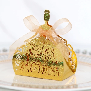 Macro detail of laser-cut gold dress-shaped gift box with peach ribbon and glitter finish