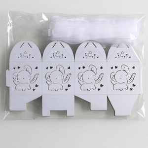 Unfolded white laser-cut favor box with elephant hollow design and white organza ribbon