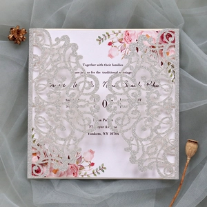 Close-up of laser-cut silver glitter wedding invitation with floral insert card