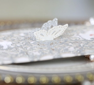 Macro detail of laser-cut 3D butterfly on silver glitter wedding invitation card