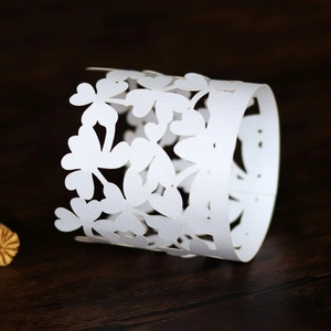 Detailed close-up of white laser-cut paper napkin ring with hollow clover pattern