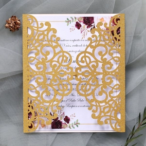 Close-up of golden laser-cut wedding invitation with glitter patterns and floral inner card