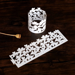 Detail view of laser-cut white clover paper napkin rings on a dark wooden surface
