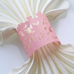 Close-up of pink laser-cut hollow heart napkin ring with pearlized finish on white satin