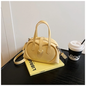Detailed close-up of a cream Boston bag with heart-shaped buckle on a library book decor
